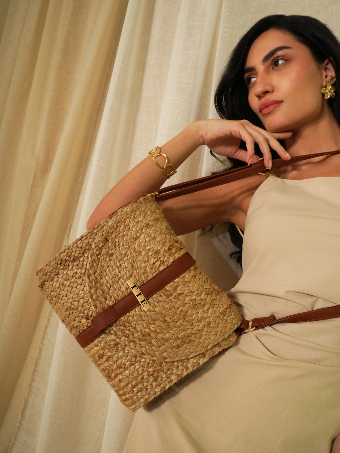 Woman holding a cubo jute sling banfgagainst a beige curtain background