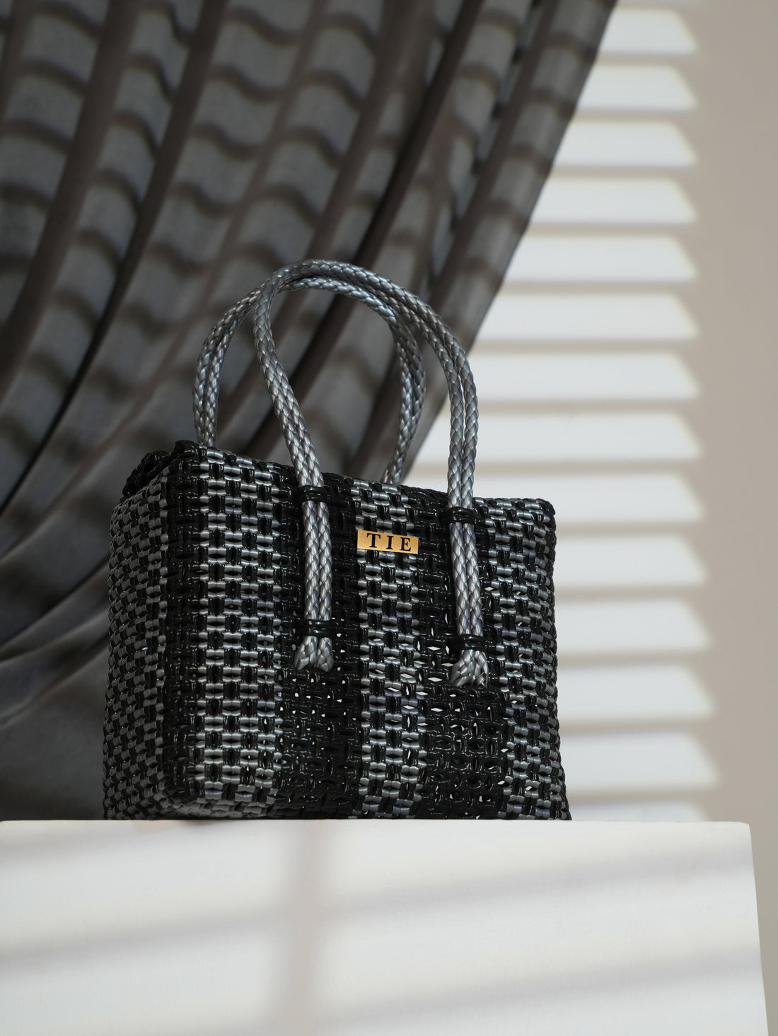 Closeweave Wire Basket - Black & Silver with a gold tag on a white surface with shadows
